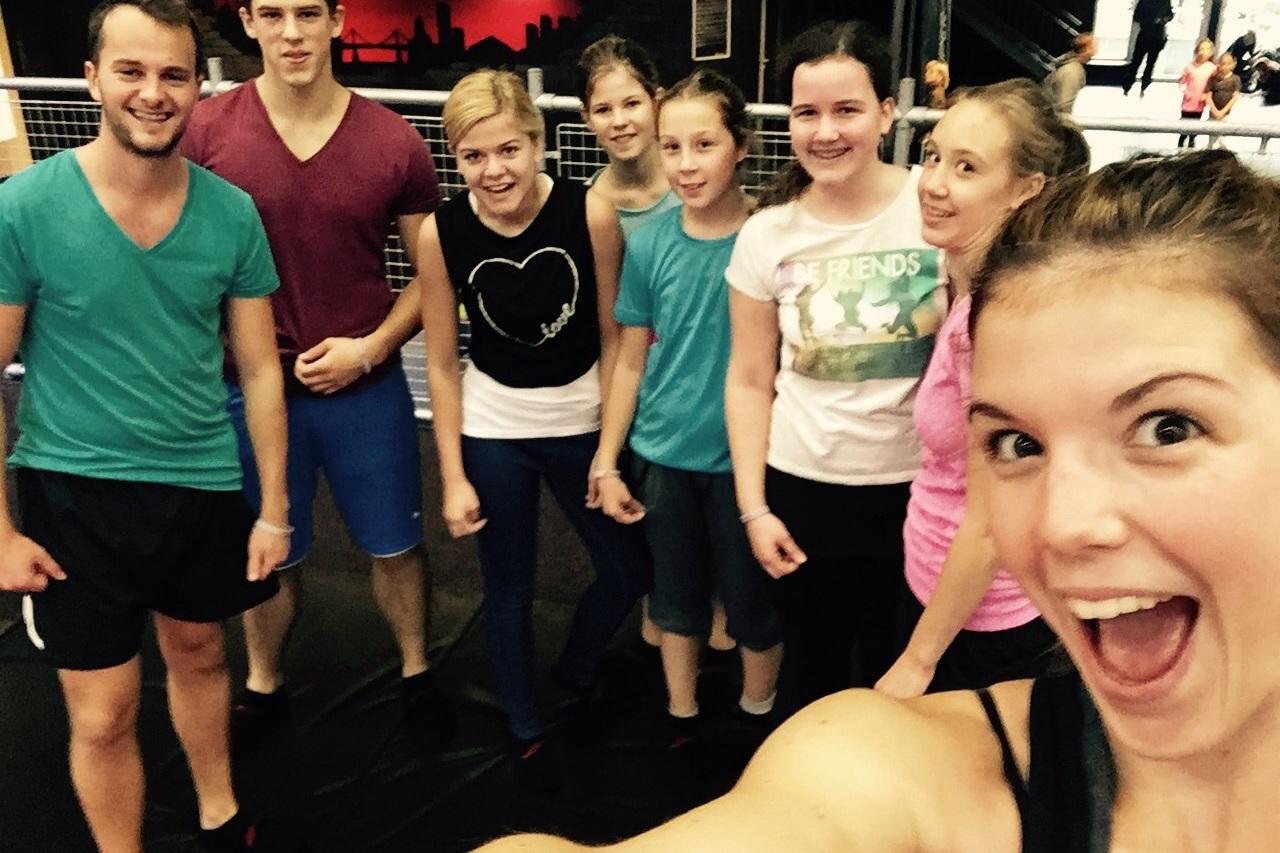 Gruppe junger Menschen posiert beim Gruppenfoto in einem Sportstudio mit Lächeln und aktiver Körperhaltung.