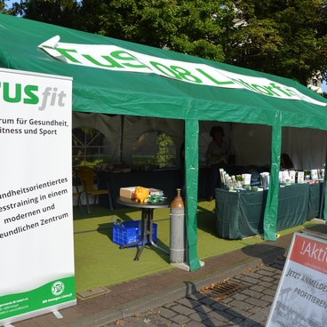 Zelt mit dem Banner &bdquo;TUSfit&ldquo; und Informationen zu Fitness und Gesundheit auf einer Veranstaltung.