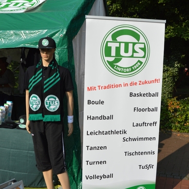 Dummie in Sportkleidung mit TUS-Logo steht vor einem Informationsstand &uuml;ber verschiedene Sportarten.