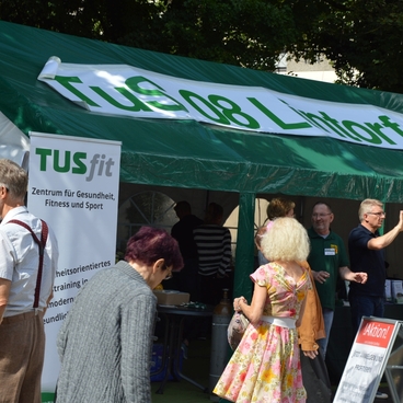 Besucher stehen vor einem Zelt mit der Aufschrift &bdquo;Tus 08 Lintorf&ldquo; und Informationen zum Thema Gesundheit und Fitness.