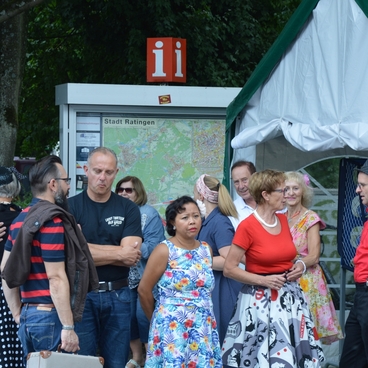 Menschen in farbenfrohen Kost&uuml;men stehen angrenzend zu einem Informationsstand in einer Stadt.