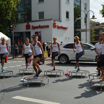 Gruppe von Frauen in Sportbekleidung springt auf Trampolinen im urbanen Umfeld. Zuschauer beobachten das Event.