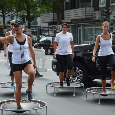 Gruppe von Frauen in Sportkleidung, die auf Mini-Trampolinen in einer urbanen Umgebung springen.