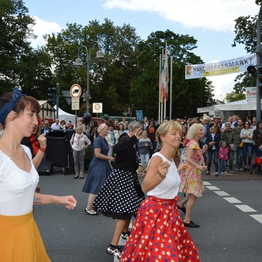 Tanzende Frauen in bunten R&ouml;cken auf einer Stra&szlig;enveranstaltung vor einer Menschenmenge im Freien.