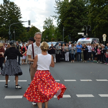 Tanzende Paare in retro Kleidern auf einer Stra&szlig;enveranstaltung, umgeben von einer Zuschauermenge.