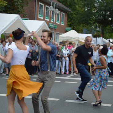 Tanzende Paare auf einem Stra&szlig;enfest, umgeben von Zuschauern und Festzelten im Hintergrund.