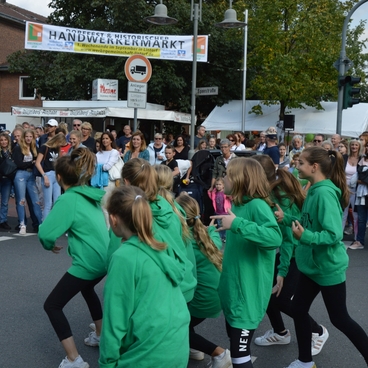 Tanzgruppe in gr&uuml;nen Kapuzenpullovern performt vor einer gro&szlig;en Zuschauermenge auf einer Stra&szlig;enveranstaltung.
