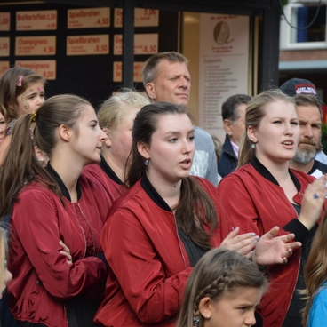 Gruppe junger Menschen in roten Jacken steht vor einem Imbissstand und applaudiert. Einige sind sichtbar begeistert.