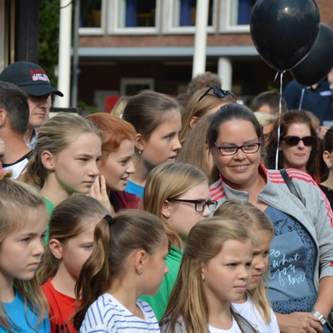 Gruppierung von Kindern und Erwachsenen bei einer Veranstaltung, einige halten schwarze Luftballons in der Hand.