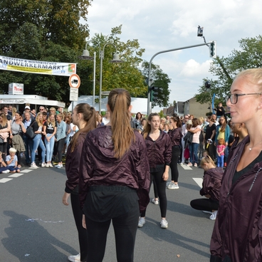 Tanzende Gruppe in sportlicher Kleidung auf einer Stra&szlig;e, Zuschauer beobachten die Darbietung beim Handwerkermarkt.