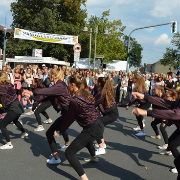 Tanzgruppe in schwarz-rosa Outfits f&uuml;hrt auf der Stra&szlig;e vor einer Zuschauermenge eine Choreografie auf.