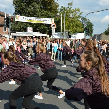 Gruppentanz von Jugendlichen in dunklen Jacken vor einer gro&szlig;en Menschenmenge auf einem Stra&szlig;enfest.