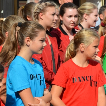 Gruppe von M&auml;dchen in bunten T-Shirts bei einer Veranstaltung, einige Zuschauer im Hintergrund.
