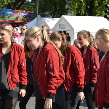 Sechs T&auml;nzerinnen in roten Jacken f&uuml;hren eine Choreografie bei einer Veranstaltung unter Publikum aus.
