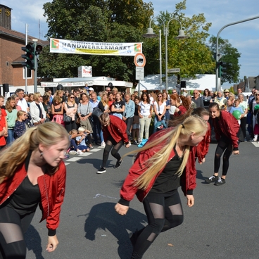 Tanzgruppe in roten Jacken f&uuml;hrt eine Auff&uuml;hrung auf der Stra&szlig;e vor einer gro&szlig;en Menschenmenge durch.