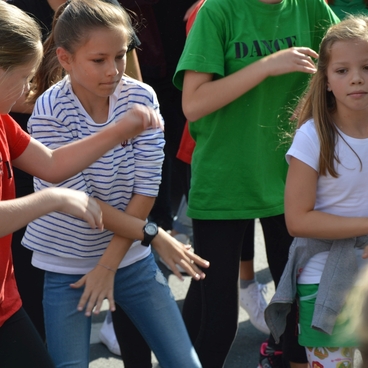 Mehrere Kinder tanzen in bunten T-Shirts auf einer Freiluftveranstaltung, mit Fokus auf drei Kinder in Aktion.