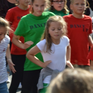 Gruppe von Kindern in bunten T-Shirts tanzt gemeinsam auf einem Au&szlig;engel&auml;nde.
