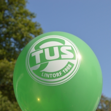 Gr&uuml;ner Ballon mit dem Logo und Schriftzug &bdquo;TUS Lintorf 1908&ldquo; vor einem blauen Himmel und gr&uuml;nen Baum.