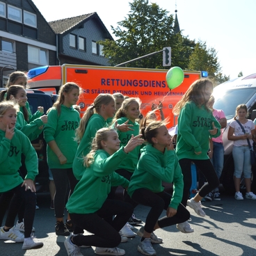 Gruppe junger T&auml;nzerinnen in gr&uuml;nen Sweatshirts f&uuml;hrt eine Choreografie vor einer Menschenmenge auf.