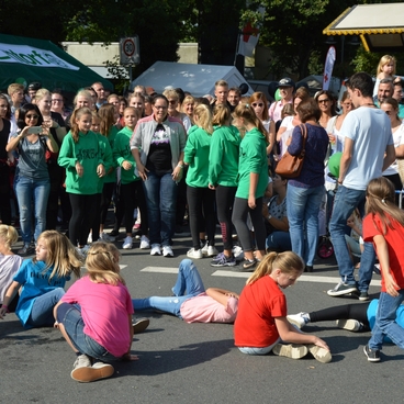 Gruppe von Kindern in bunten T-Shirts f&uuml;hrt eine Darbietung auf der Stra&szlig;e vor einer Menge von Zuschauern auf.