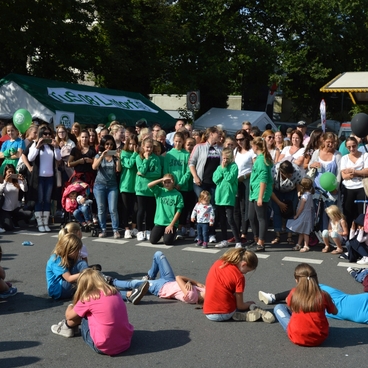 Mehrere Kinder in T-Shirts f&uuml;hren eine Auff&uuml;hrung auf der Stra&szlig;e vor einer gro&szlig;en Menschenmenge durch.