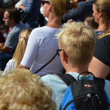 Menschenmenge bei einer Veranstaltung, mehrere Personen sind von hinten sichtbar, darunter Kinder und Erwachsene.