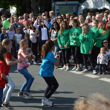Gruppe von Kindern in bunten T-Shirts tanzt vor einer Zuschauermenge auf der Stra&szlig;e.
