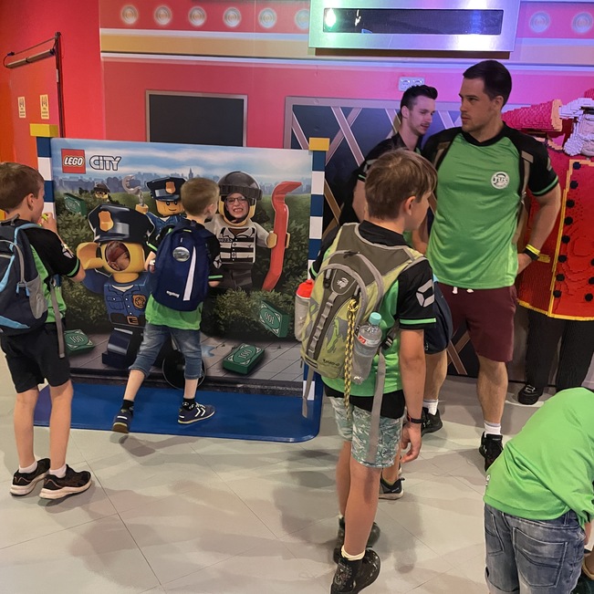 Zwei Kinder und ein Erwachsener stehen vor einer LEGO City-Attraktion in einem bunten Indoor-Spielplatz.