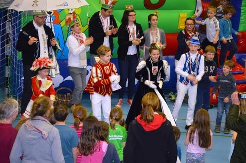 Karnevalsumzug in einer Turnhalle mit bunt kost&uuml;mierten Kindern und Erwachsenen, die zusammen feiern und tanzen.