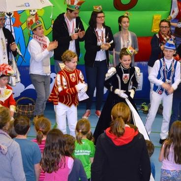Karnevalsumzug in einer Turnhalle mit bunt kost&uuml;mierten Kindern und Erwachsenen, die zusammen feiern und tanzen.