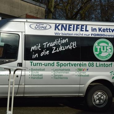Wei&szlig;er Transporter mit Werbung f&uuml;r den Turn- und Sportverein 08 Lintorf e.V. und Ford, geparkt vor einem Geb&auml;ude.