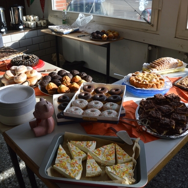 Tisch mit verschiedenen s&uuml;&szlig;en Backwaren, darunter Donuts, Kuchen und Pl&auml;tzchen, neben Getr&auml;nken in Gl&auml;sern.
