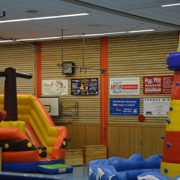 Luftige Spielger&auml;te in einer Halle: eine Rutsche und ein Leuchtturm in bunten Farben auf einem blauen Spielbereich.
