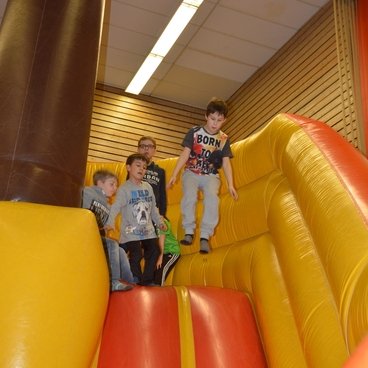 F&uuml;nf Kinder klettern auf einer bunten H&uuml;pfburg und bereiten sich auf das Herunterrutschen vor.
