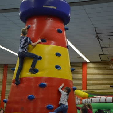 Zwei Kinder klettern auf einem bunten, aufblasbaren Kletterturm in einer Sporthalle.