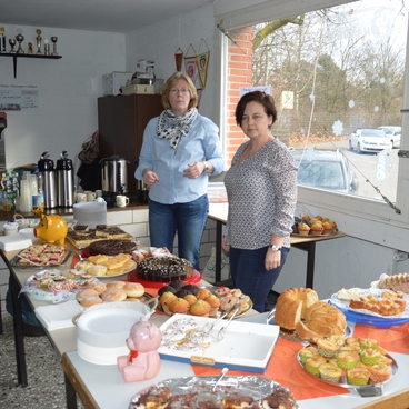 Zwei Frauen stehen an einem Tisch, der mit verschiedenen Kuchen und Geb&auml;ck dekoriert ist. Im Hintergrund stehen Pokale.