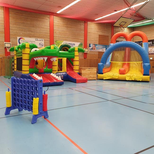 Bunte H&uuml;pfburgen und ein Verbindungsspiel stehen in einer Sporthalle mit blauer Bodenfl&auml;che.