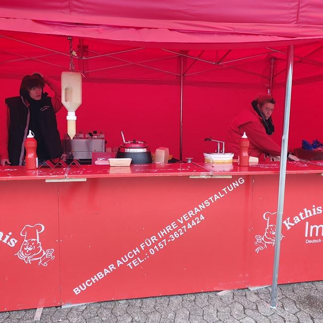 Zwei Verk&auml;ufer stehen an einem roten Imbissstand mit verschiedenen Zutaten und Ger&auml;ten.