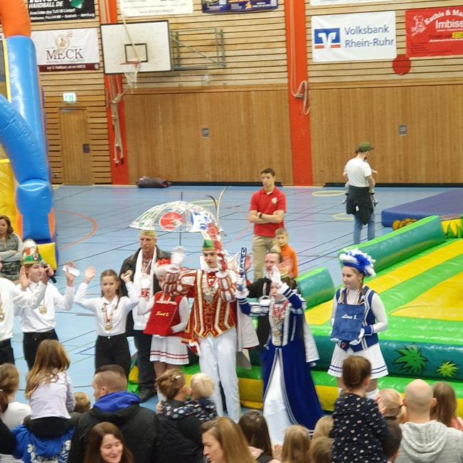Gruppenszene mit kost&uuml;mierten Personen und Kindern in einer Sporthalle, im Hintergrund eine H&uuml;pfburg und Spielecke.