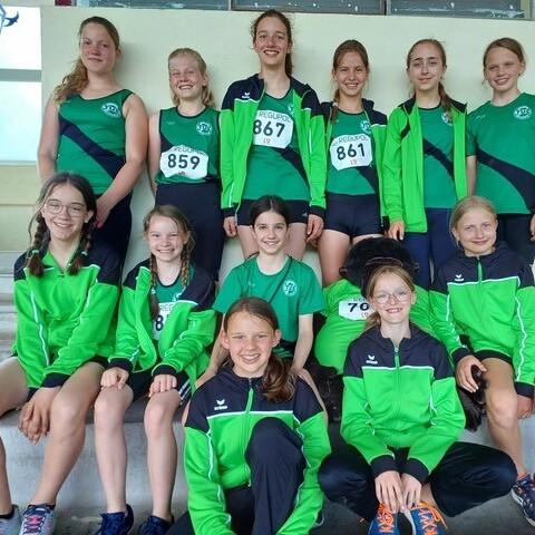 Gruppenfoto von zw&ouml;lf Jugendlichen in Sportbekleidung mit Vereinsnummern, l&auml;chelnd auf einer Treppe posierend.