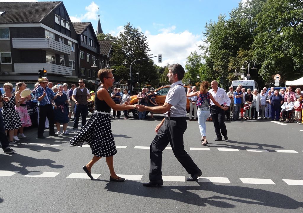 Tanzen von Paaren auf einer Stra&szlig;e w&auml;hrend einer Sommerveranstaltung, umgeben von Zuschauern in festlicher Stimmung.