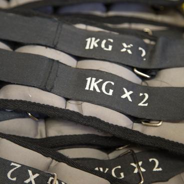 Reihe von Gewichtsmanschetten mit der Beschriftung &bdquo;1KG x 2&ldquo; auf einer flachen Oberfl&auml;che.