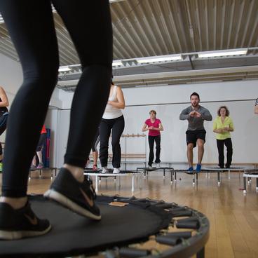 Group fitnesskurs auf Trampolinen, Teilnehmer springen in einem hellen Raum mit Holzboden.