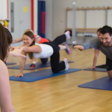 Gruppe von Menschen in Sportkleidung, die auf Matten &Uuml;bungen zur Kr&auml;ftigung der R&uuml;ckenmuskulatur durchf&uuml;hren.