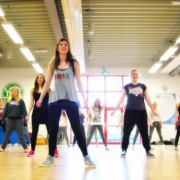 Gruppe von T&auml;nzerinnen in Sportkleidung bewegt sich synchron in einem hellen Tanzstudio.
