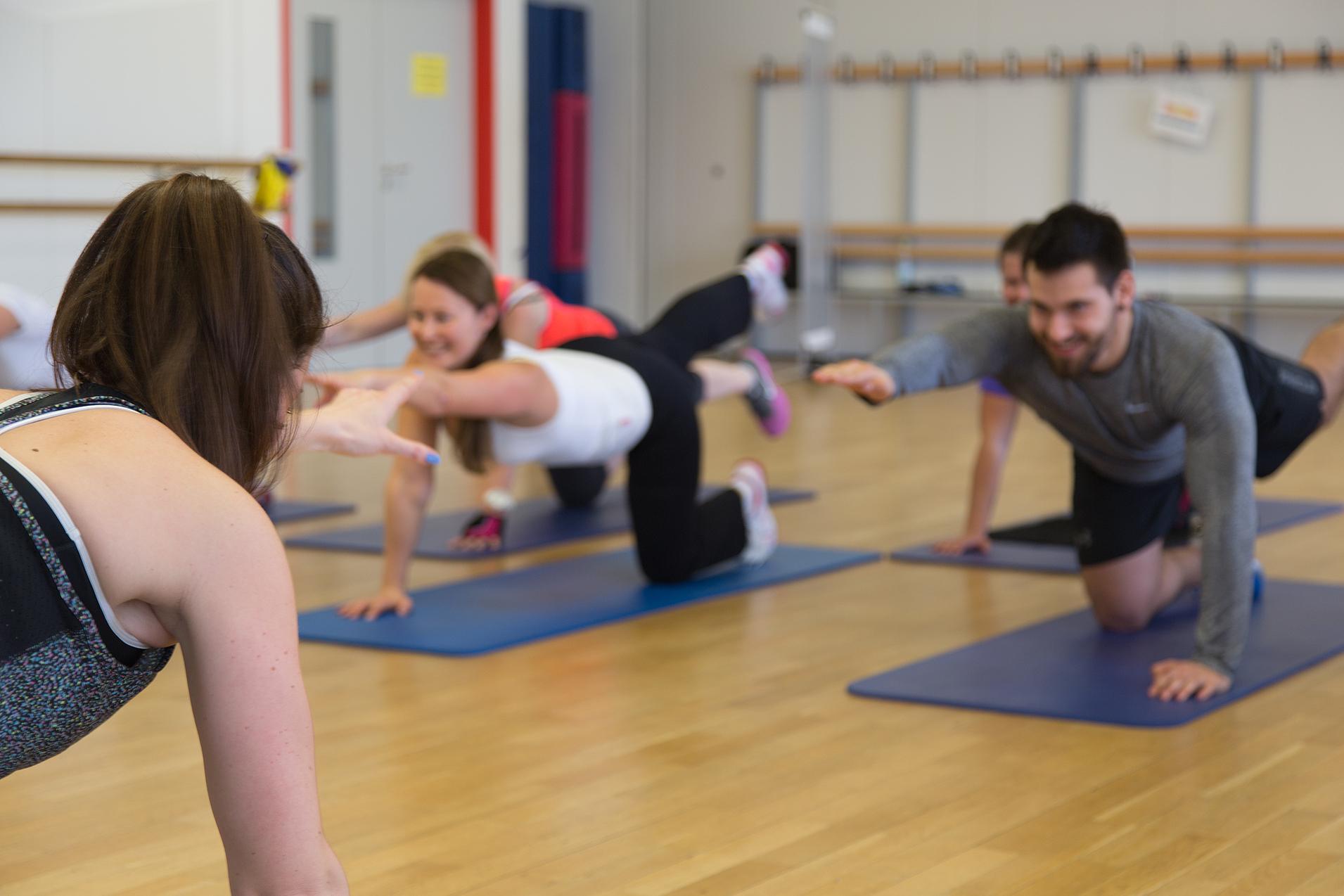 Gruppe von Menschen in Sportkleidung, die auf Matten Übungen zur Kräftigung der Rückenmuskulatur durchführen.