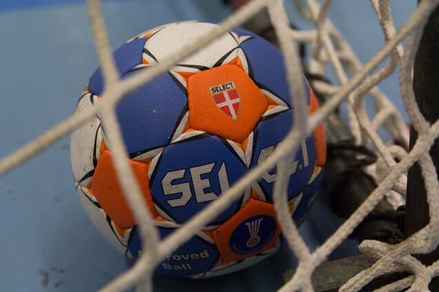 Nahaufnahme eines Handballs mit blau-orange Farbgebung, der im Netz eines Handballtors liegt.