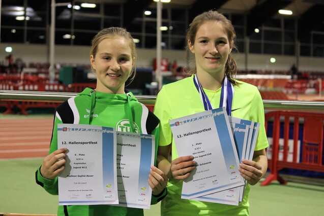 Zwei junge Sportlerinnen halten Urkunden und eine Medaille nach dem Hallensportfest in einer Sporthalle.