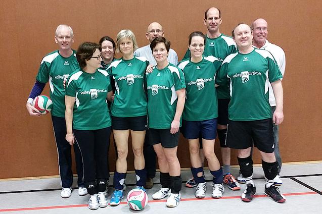 Gruppennfoto eines Volleyballteams in gr&uuml;nen Trikots, umgeben von Volleyballb&auml;llen in einer Sporthalle.