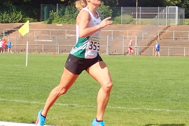 Athletin mit Startnummer 353 l&auml;uft energisch auf einer Laufbahn, im Hintergrund sind Zuschauer und Trib&uuml;nen sichtbar.